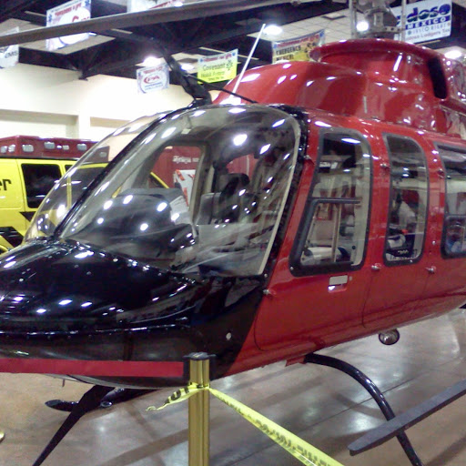 A helicopter on display inside the Exhibit Hall during a trade show, sponsor banners hanging from the ceiling and a rescue vehicle parked beside it.