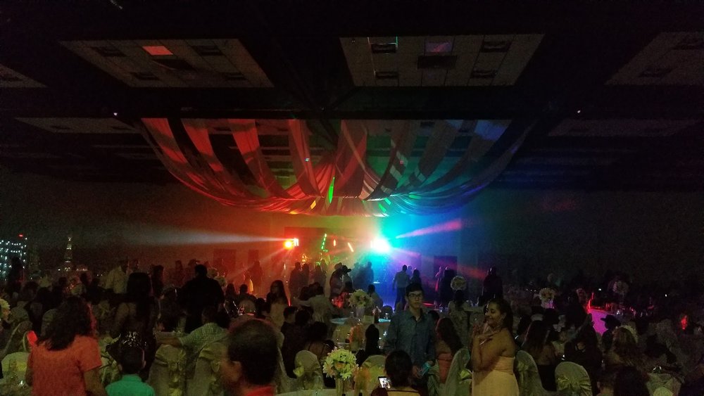 A packed evening event under a white-draped ceiling lit by rainbow-colored laser beams.