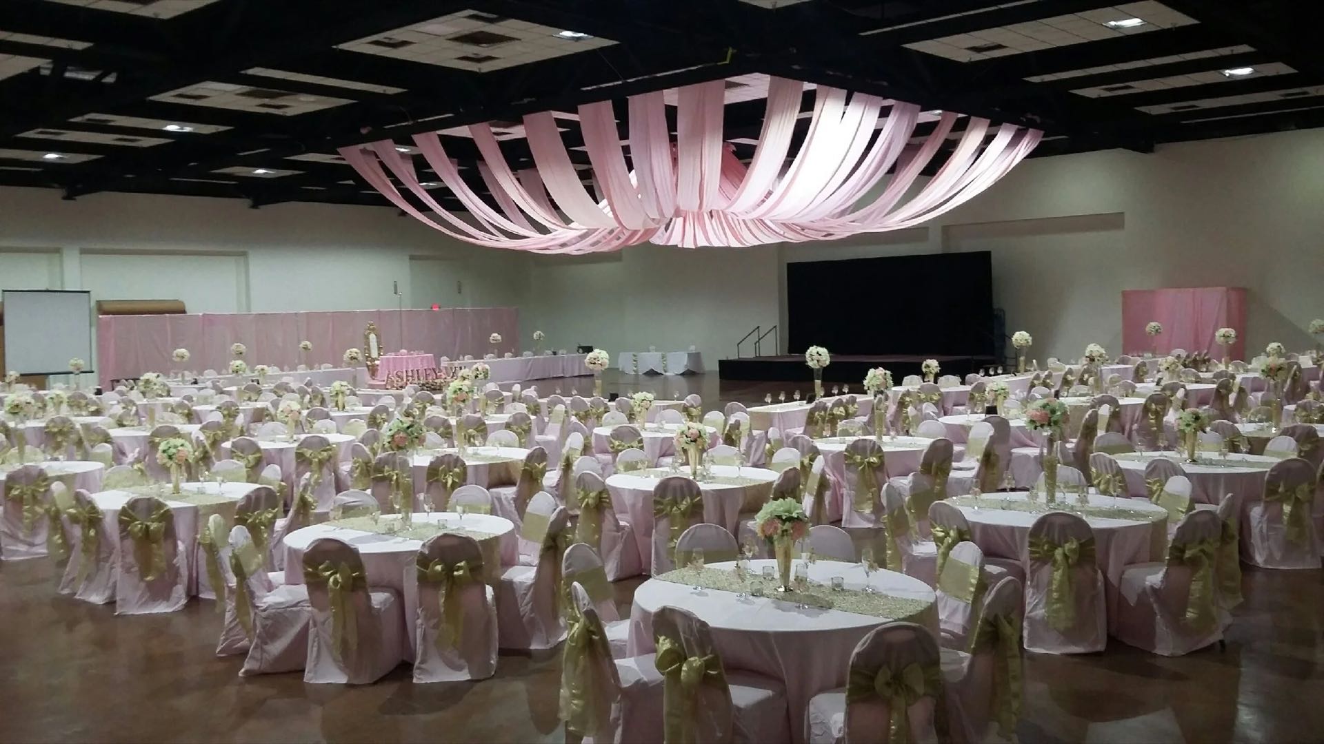 A full banquet layout in the Exhibit Hall: round tables with pink linens and gold chair sashes under a draped fabric canopy, seating for hundreds.