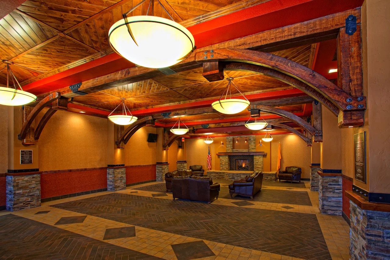 The lobby shared with the adjacent hotel: heavy timber trusses, a stone fireplace, and leather armchairs.