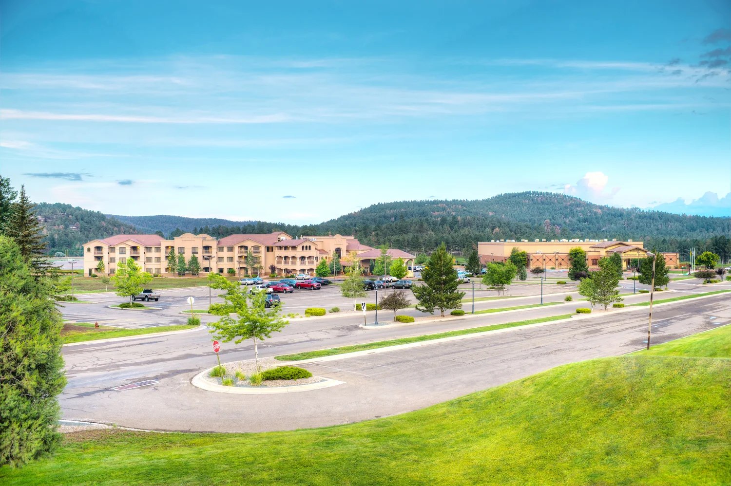 Aerial view of MCM Eleganté Lodge & Resort directly beside the Ruidoso Convention Center, forested mountains behind both buildings.