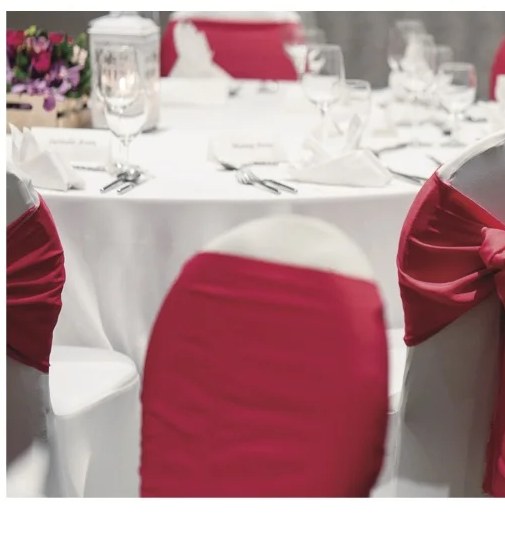 A formal wedding table setting with white linens, crystal glassware and burgundy chair sashes.